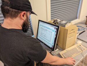 A man in a baseball cap using a vintage computer.