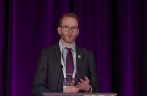 A man in a suit speaking at a podium.