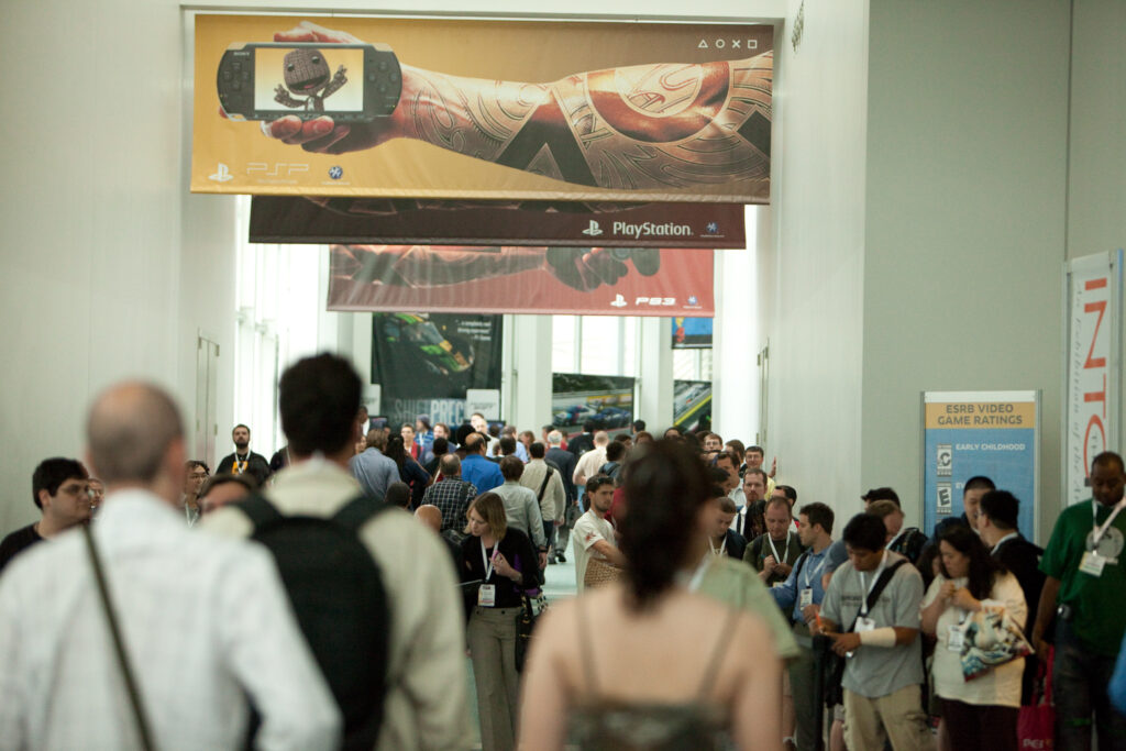 A tight shot of a hallway at E3 2009. A large banner for the PSP looms over the packed crowd.