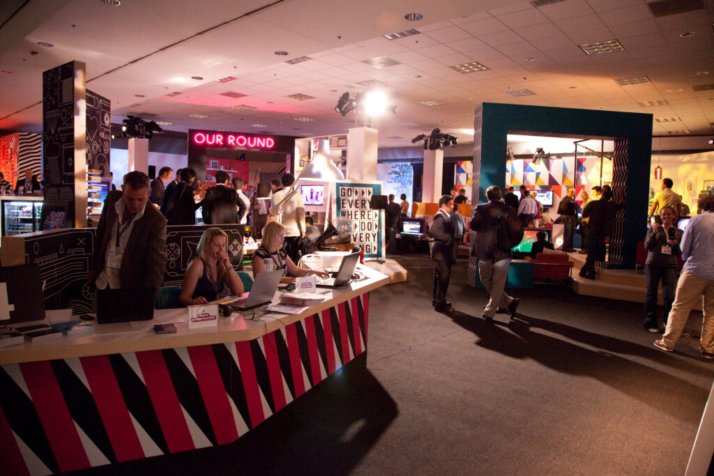 A view of a crowded but cozy lounge area, set up in what appears to be a medium-sized function room. There are various configurations of couches set up to play video games.