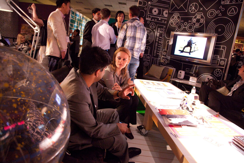 Two people meeting at a small breakout table in a lounge room. They are surrounded by oversized PlayStation-theme decor.