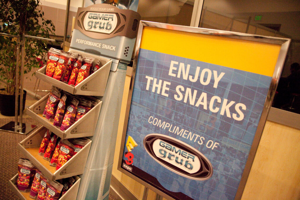 A display of Gamer Grub Performance Snack. An E3-branded sign reads "Enjoy the snacks, compliments of Gamer Grub."