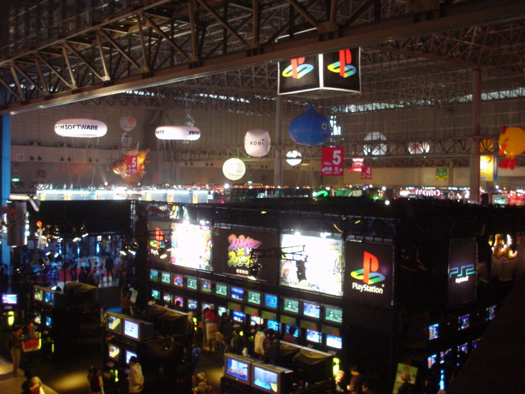 A view of the main hall at Tokyo Game Show Spring 2000. Visible products companies include Pac-Man, Dragon Quest, the Sega Dreamcast, Tecmo, and FromSoftware.
